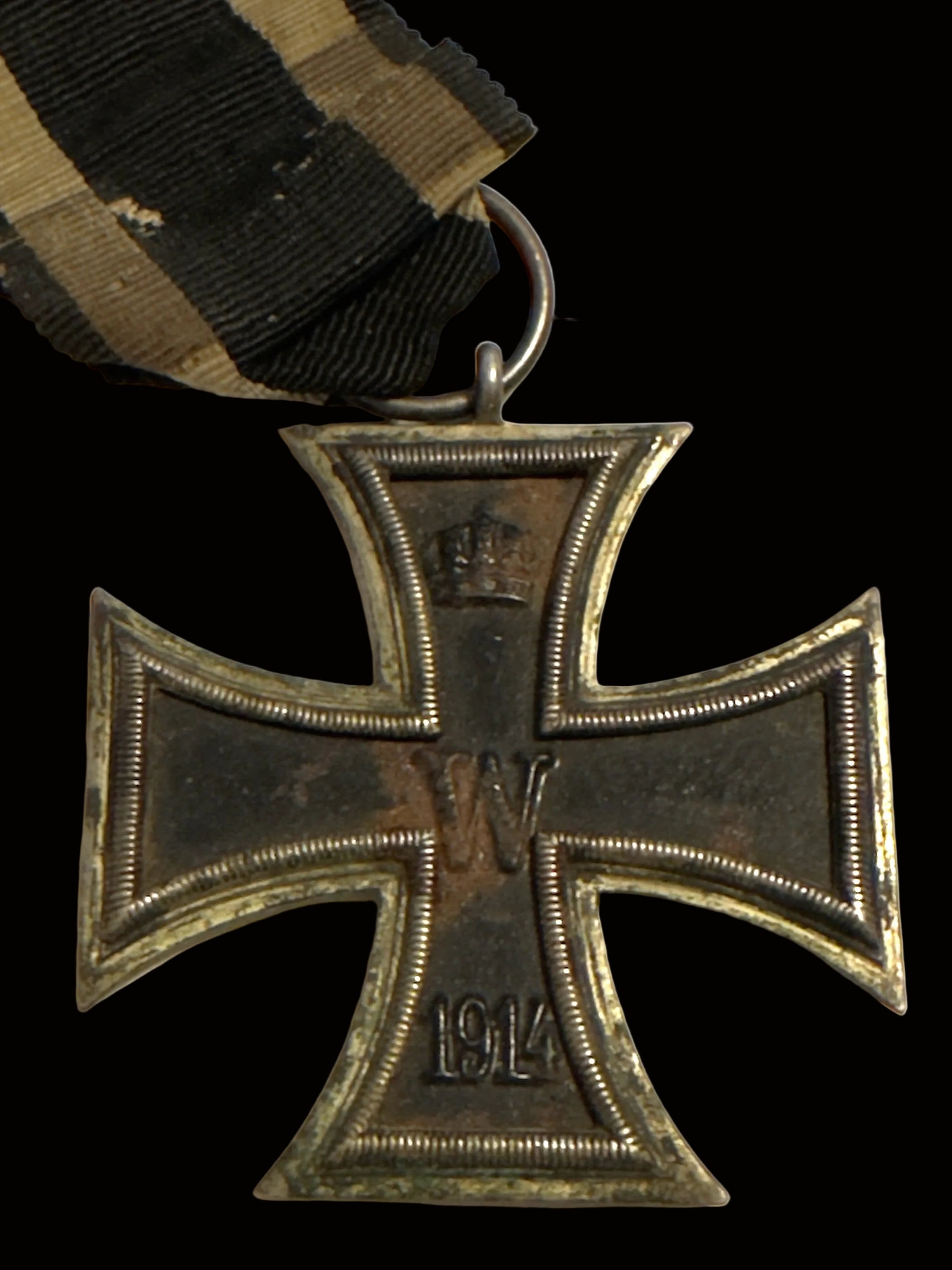 A close-up of a World War I German Iron Cross 1st Class medal with a black and khaki striped ribbon, on a plain off-white background.
