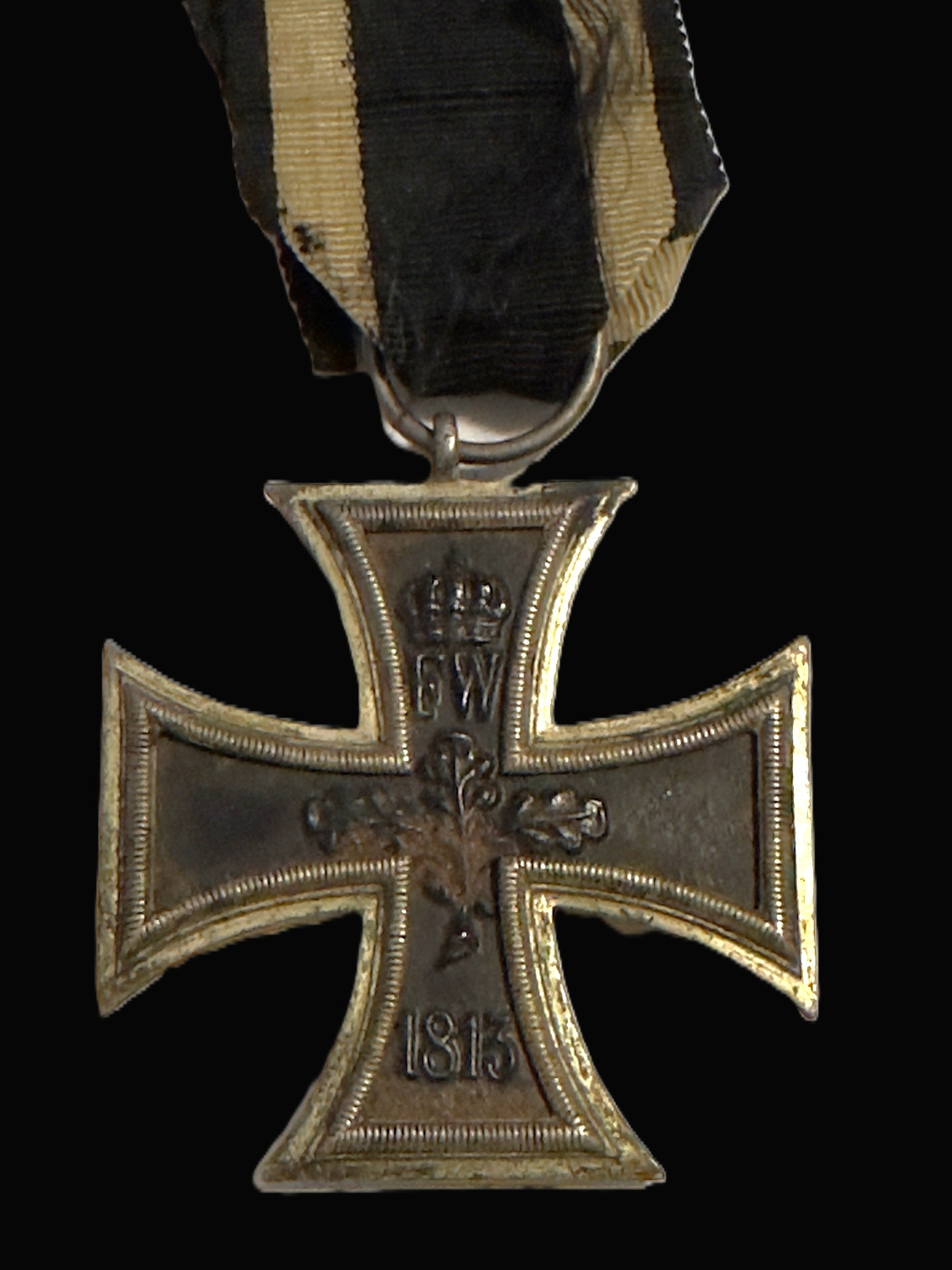 A German World War I Iron Cross 1st Class medal with a black and beige striped ribbon, shown against a solid black background.