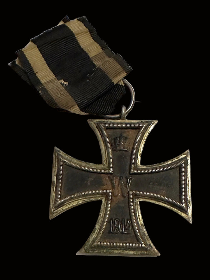 A vintage German Iron Cross 1914 medal with a black and khaki striped ribbon, displayed on a plain off-white background.