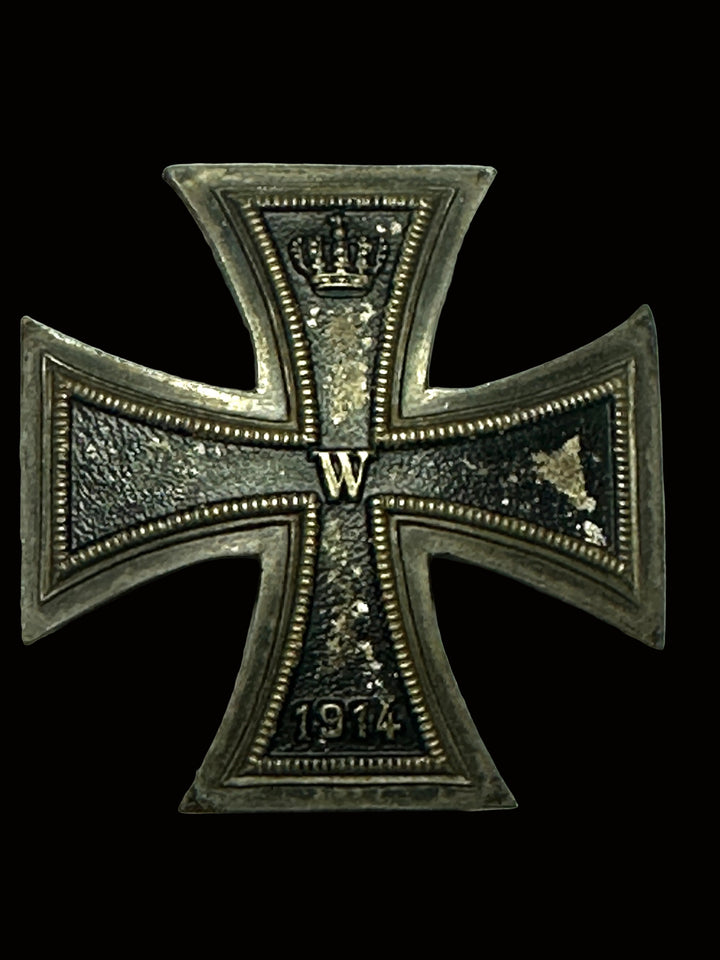 A vintage German Iron Cross 1914 medal with a 'W' for Wilhelm II and the year '1914' engraved on it, displayed on a light gray textured background.