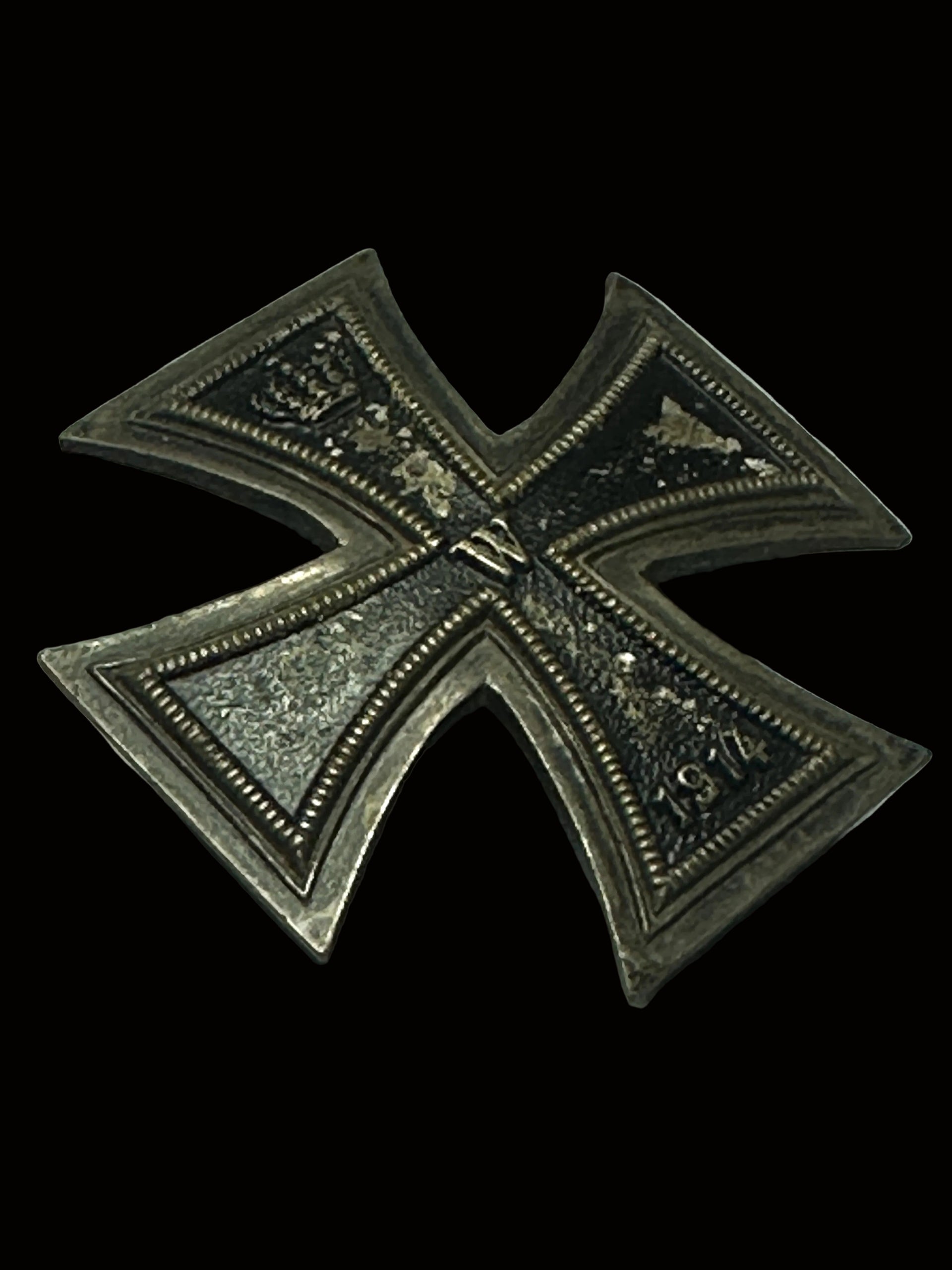 A vintage German Iron Cross 1914 medal pin, featuring a silver-toned metal cross with dark oxidized details and a central crown emblem, resting on a gray textured surface.
