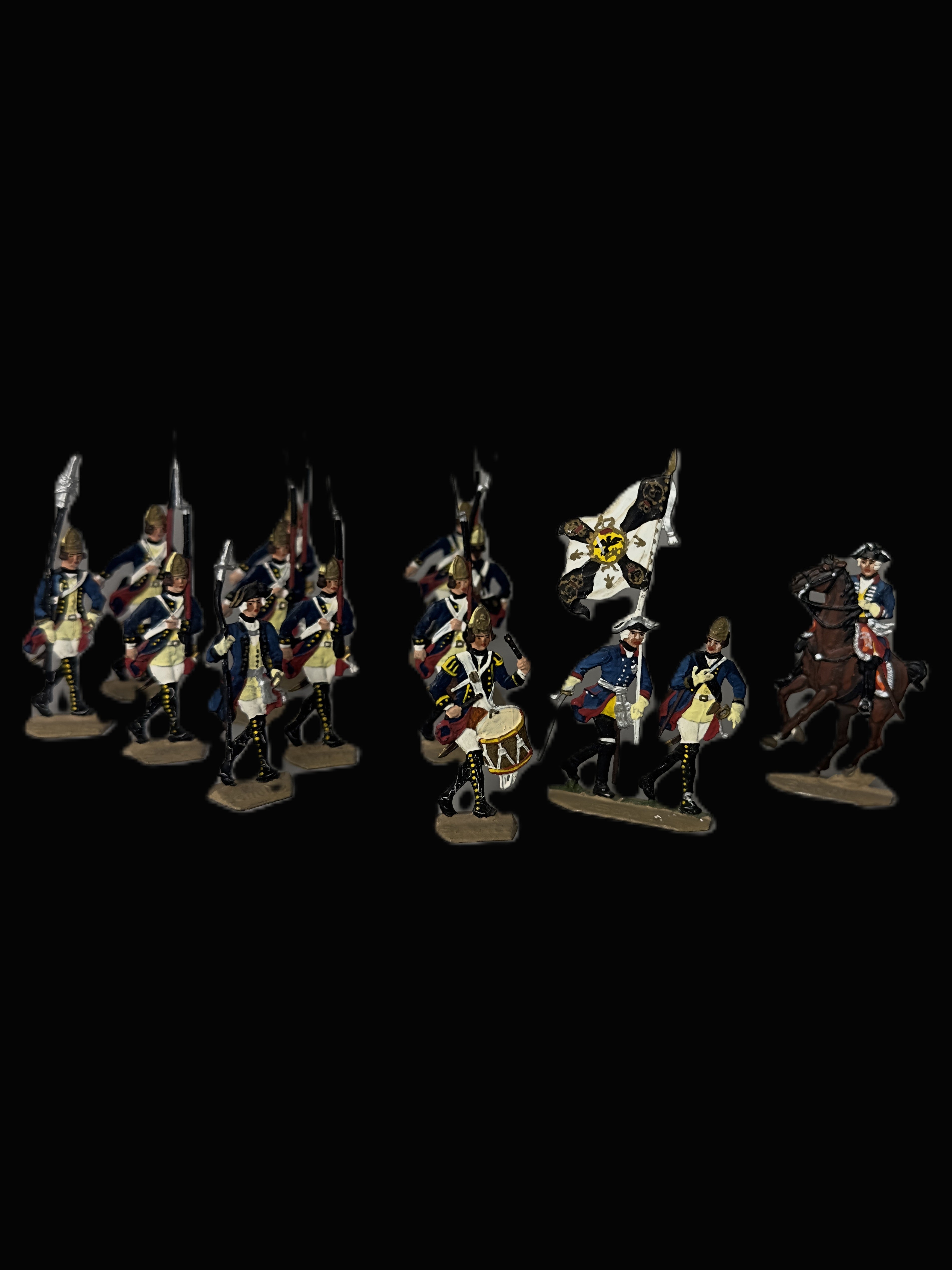 A set of painted historical military miniature figurines, including soldiers with rifles, a flag bearer, and a mounted soldier on a horse, displayed against a solid black background.