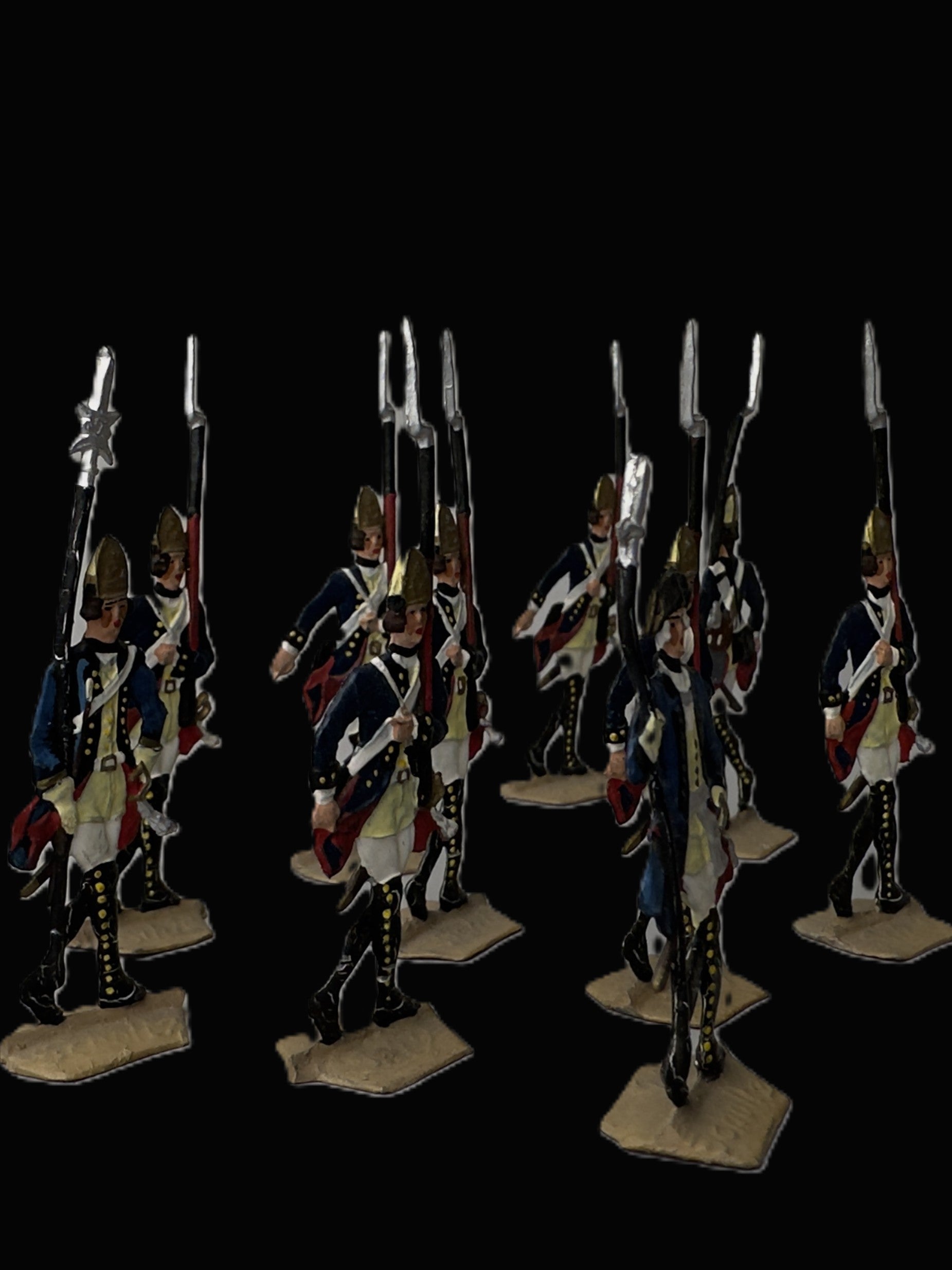 A set of miniature historical military figures dressed in blue, white, and red uniforms with gold details, holding long rifles on beige bases against a black background.