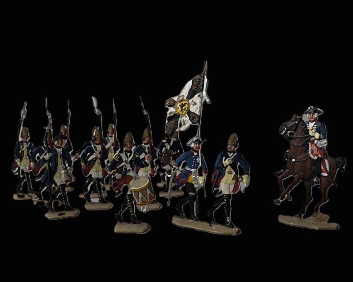 A set of miniature historical military figurines on a solid black background. The collection includes soldiers in blue and white uniforms with red accents, a drummer, a flag bearer, and a mounted officer on a brown horse.