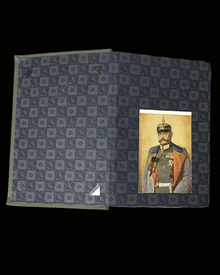 A vintage hardcover book or album cover lying flat on a light gray surface. The cover features a dark blue and gray geometric pattern on the left side and a portrait of a historical military figure on the right side.