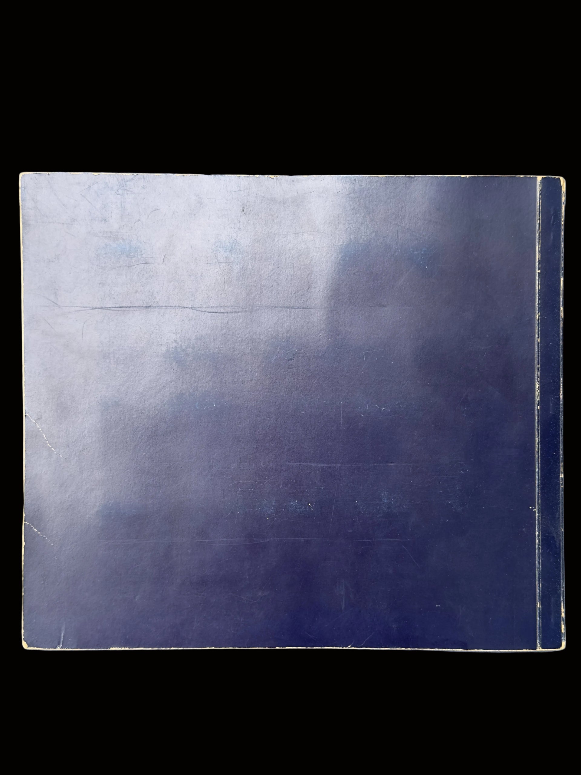 A square dark blue-gray tile or panel with a glossy finish, showing some wear, scratches, and a slight sheen, placed on a textured light blue-gray surface.