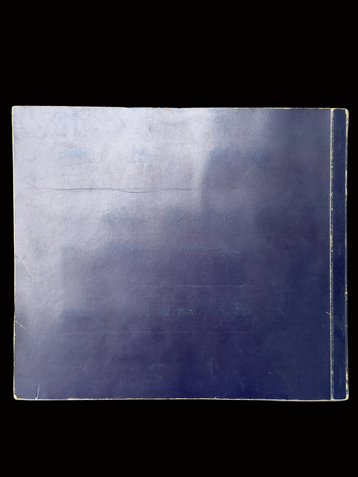 A square dark blue-gray tile or panel with a glossy finish, showing some wear, scratches, and a slight sheen, placed on a textured light blue-gray surface.