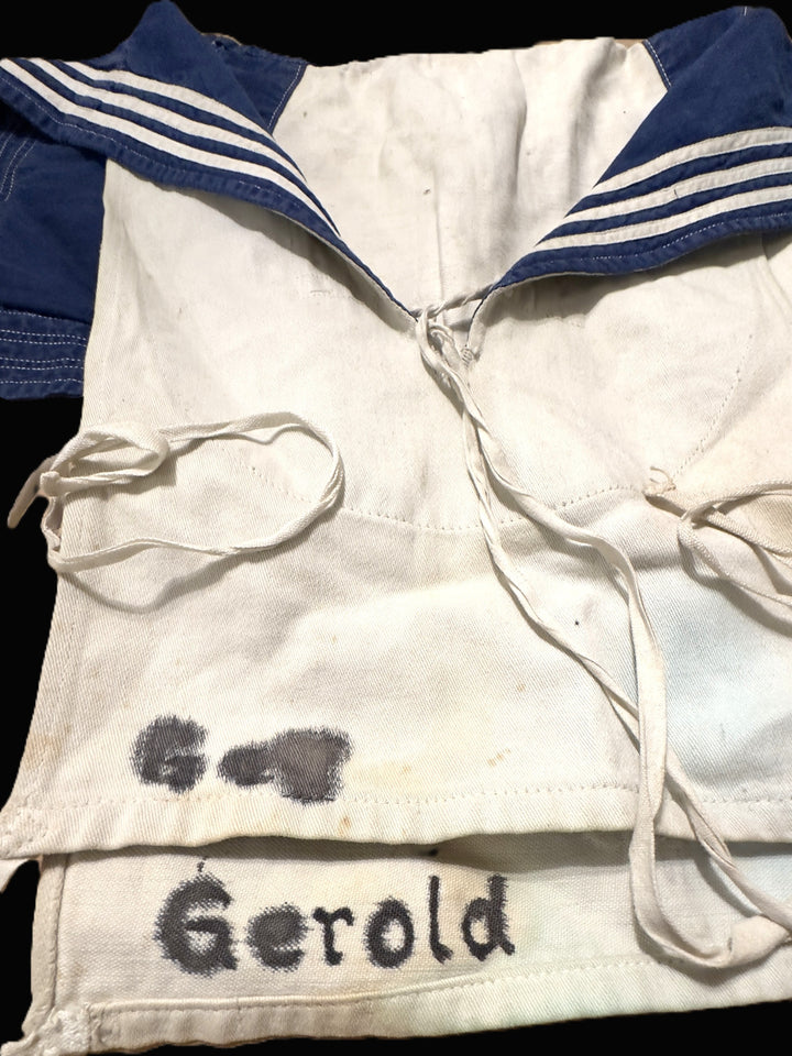A vintage white sailor-style shirt with blue collar trim and white stripes, featuring a cream cord and the name 'Gerold' embroidered in black on the front.