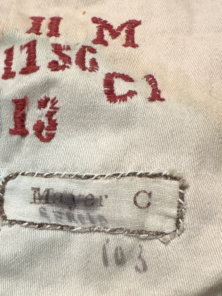 Close-up of a vintage off-white denim or canvas garment showing red embroidered markings and a sewn-on label reading 'Mayer C'.