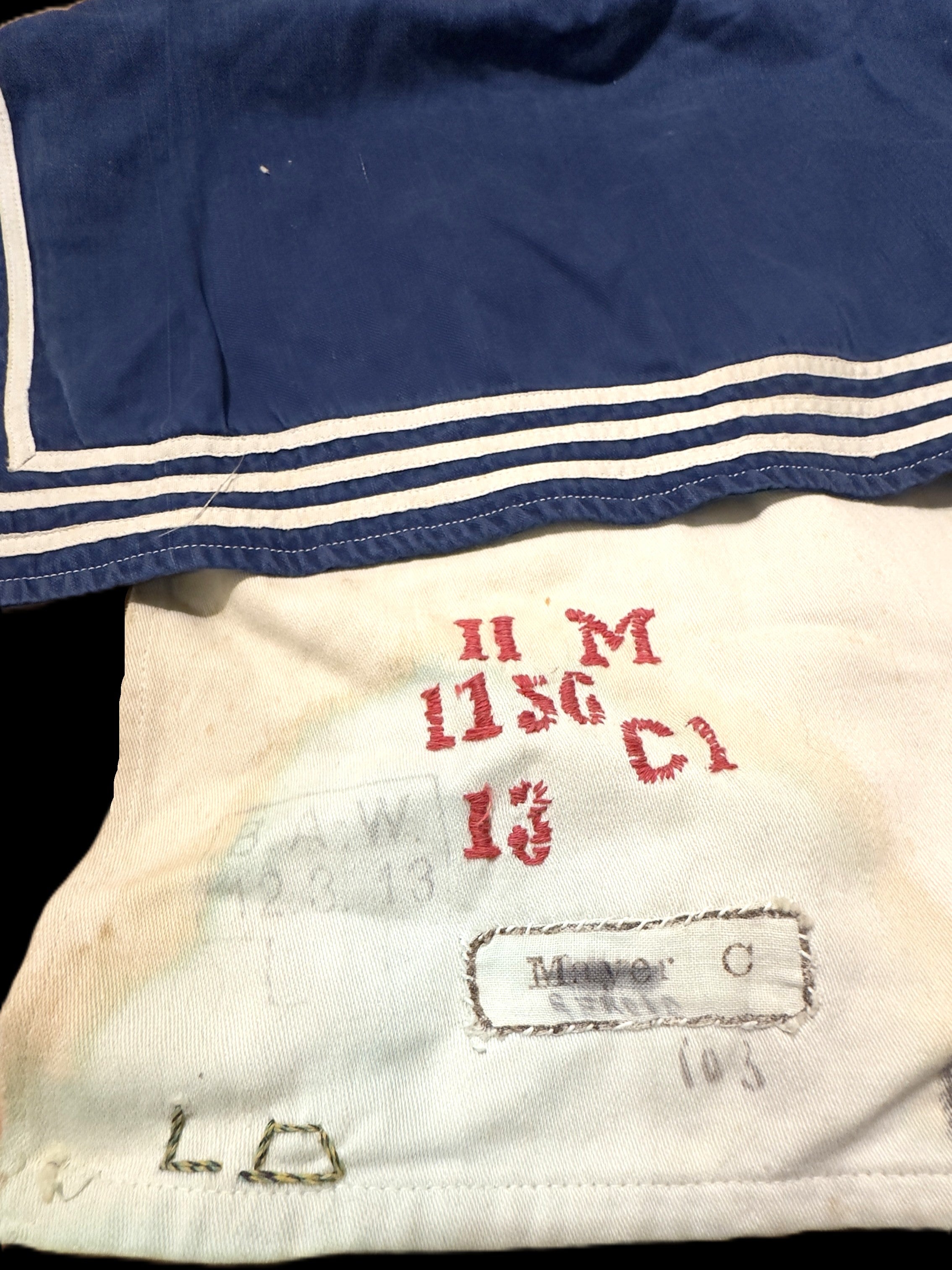 Close-up of a vintage navy blue sailor collar garment with white stripes, showing a cream-colored inner lining with red stamped markings and a sewn-in label.