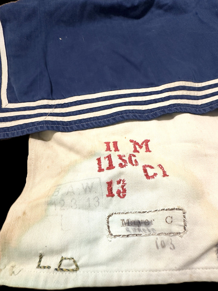 Close-up of a vintage navy blue sailor collar garment with white stripes, showing a cream-colored inner lining with red stamped markings and a sewn-in label.