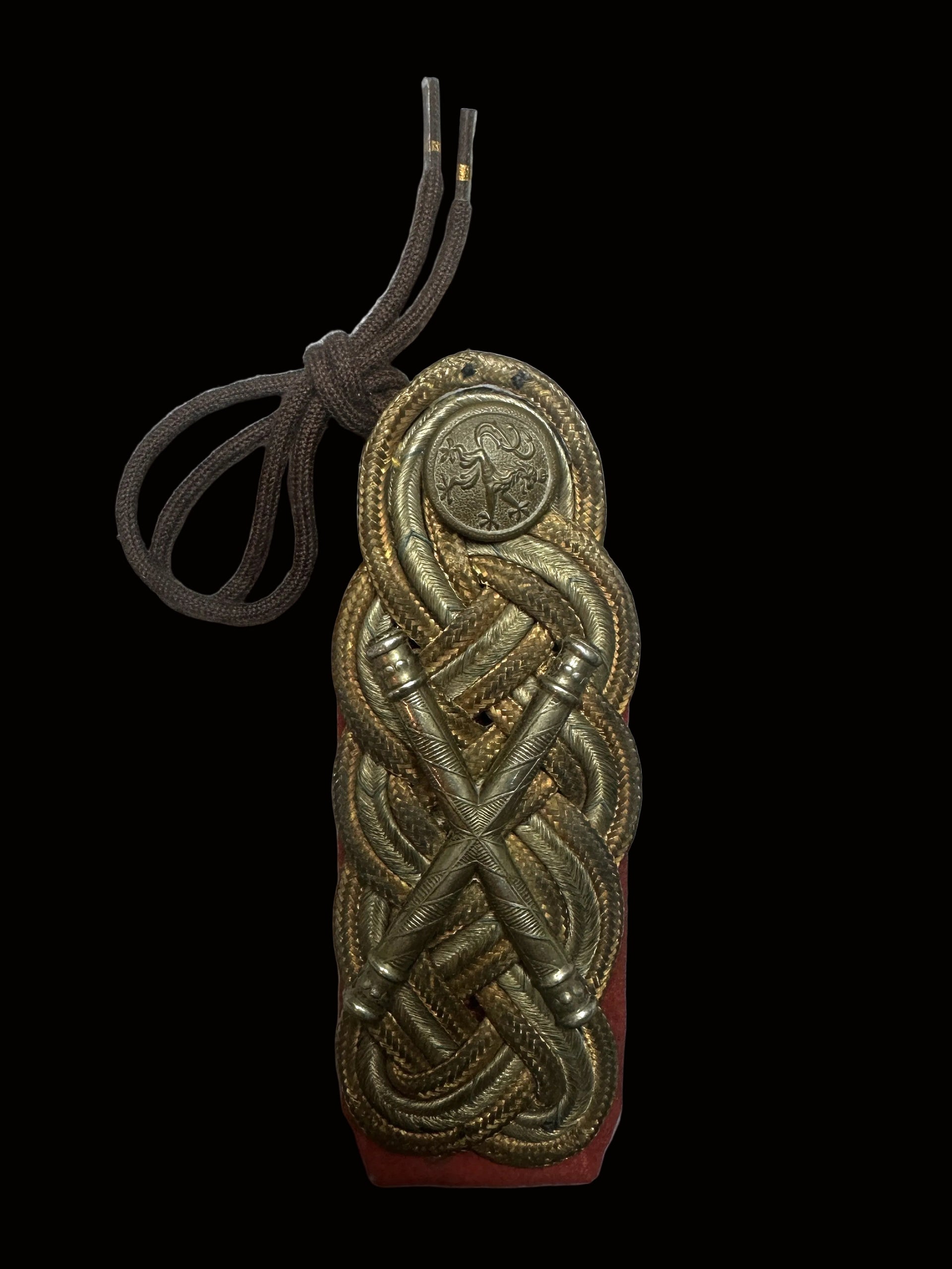An ornate brass military rank insignia with braided details and a brown cord, displayed on a red backing against a light gray background.