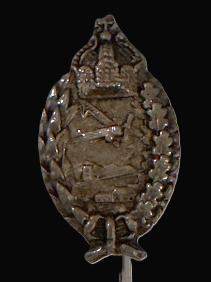 An antique silver-toned enamel pin or badge with an embossed military or historical emblem, featuring a wreath and central crest, shown against a solid black background.